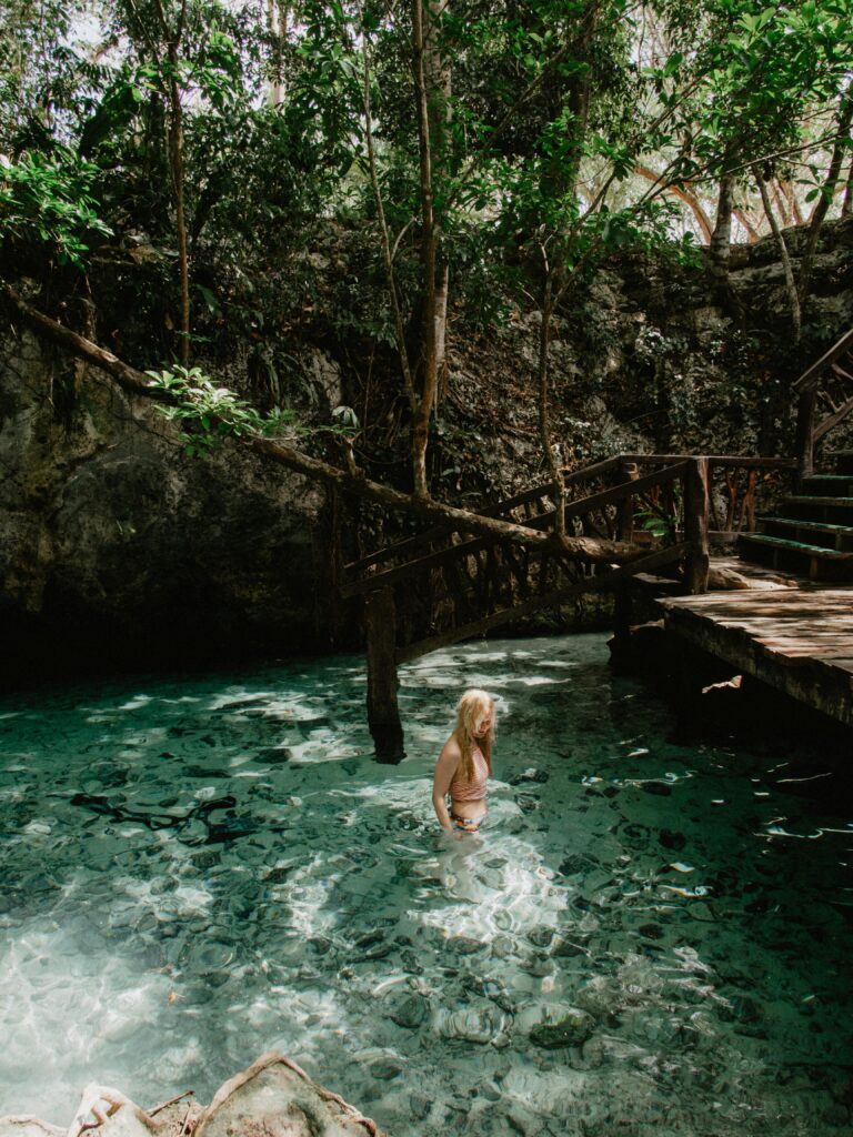 Woman enjoys a peaceful swim in a lush Mexican cenote surrounded by nature.